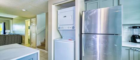 A compact kitchen with a stainless steel refrigerator, a built-in washer-dryer unit, and a blender on the countertop.
