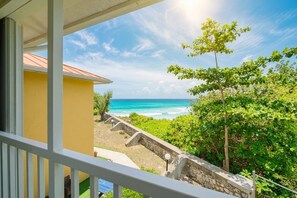 A balcony with a view of the ocean, a stone wall, and a yellow building.