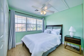 A bedroom with a bed, a nightstand, a lamp, a ceiling fan, and a window with blinds. - Oceanfront Peace 2BR with Wave Views (Patricks Island)