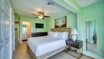 A bedroom with a bed, bedside table, lamp, ceiling fan, and a painting on the wall.