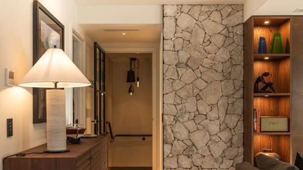 A modern living room with a stone accent wall, a wooden console table with a lamp, and a bookshelf with decorative items. - 11 Earl by MajorDomo | Modern 2-Bedroom Apartment in the Heart of Downtown Queenstown, Steps to Lake, Dining & Shops (Queenstown)