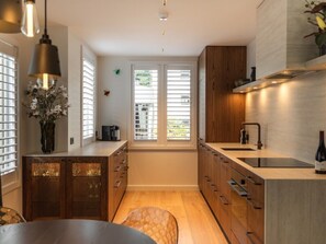 Een kleine keuken met houten kastjes, een inbouwspoelbak en een raam met zonwering.