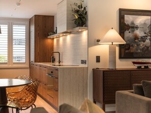 A modern kitchen with wooden cabinets, a built-in island, and a dining area with a glass table and chairs. - 11 Earl by MajorDomo | Modern 2-Bedroom Apartment in the Heart of Downtown Queenstown, Steps to Lake, Dining & Shops (Queenstown)