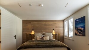 A bedroom with a bed, two wall-mounted lights, a window with blinds, and a painting on the wall. - 11 Earl by MajorDomo | Modern 2-Bedroom Apartment in the Heart of Downtown Queenstown, Steps to Lake, Dining & Shops (Queenstown)
