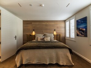 A bedroom with a bed, two wall-mounted lights, a window with blinds, and a painting on the wall. - 11 Earl by MajorDomo | Modern 2-Bedroom Apartment in the Heart of Downtown Queenstown, Steps to Lake, Dining & Shops (Queenstown)