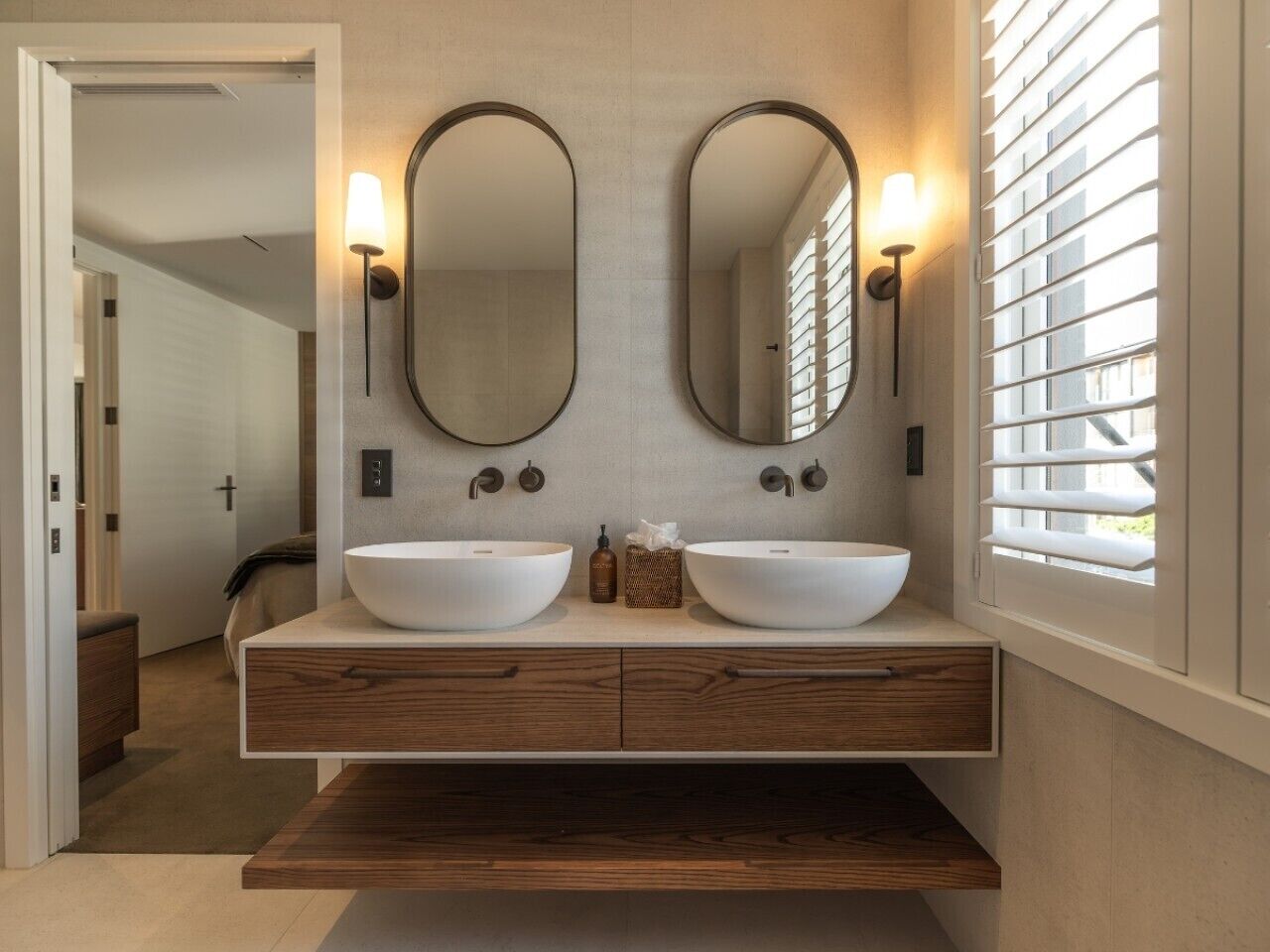A modern bathroom with two large white sinks, wooden vanity, and wall-mounted lights.