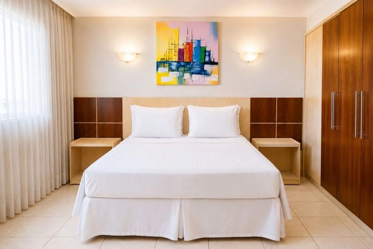 A hotel room with a large bed, two bedside tables, a wooden wardrobe, and a cityscape painting on the wall.