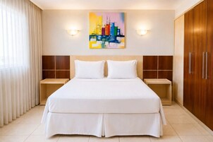 Habitación de hotel con una cama grande, dos mesitas de noche, un armario de madera y un cuadro de paisaje urbano en la pared.