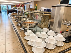 Montaje de bufé con múltiples estaciones de servicio, incluyendo una máquina de café y diversos recipientes de comida.