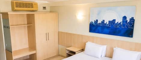 A hotel room with a bed, a wardrobe, a nightstand, and a cityscape painting on the wall.