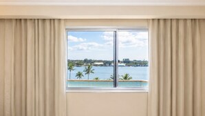 Una habitación con un ventanal, cortinas y vistas a un cuerpo de agua con palmeras.
