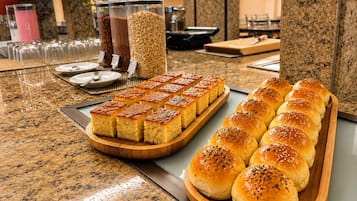 Mesa de buffet com diversos alimentos, incluindo pães e uma bandeja de doces.