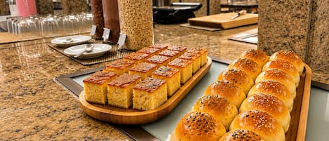 A buffet table with various food items, including bread rolls and a tray of baked goods.