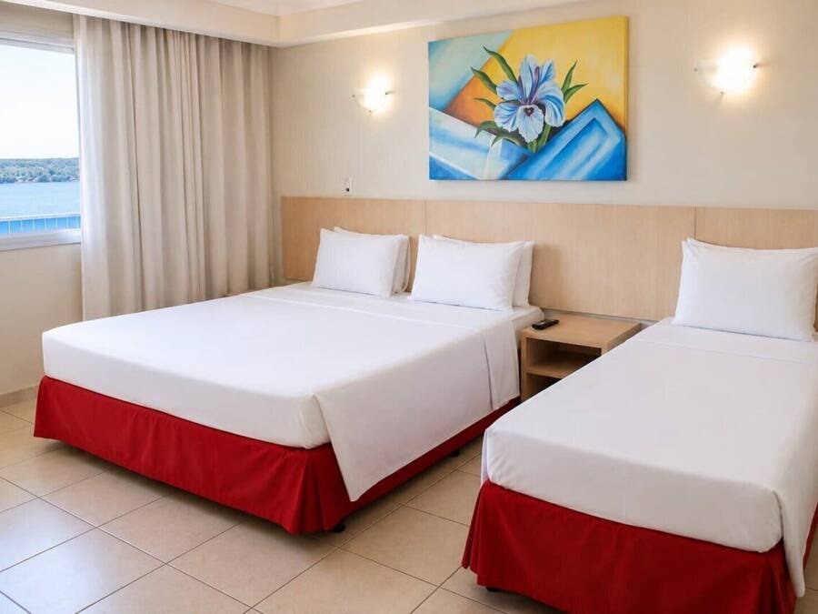 A hotel room with two beds, a painting on the wall, and a window with curtains.
