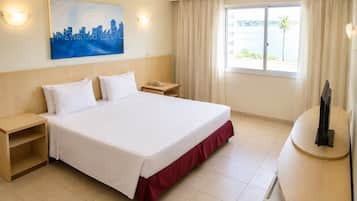 Ein Hotelzimmer mit Bett, Nachttischen, Schreibtisch, Stuhl, einem Gemälde und einem Fenster mit Blick.