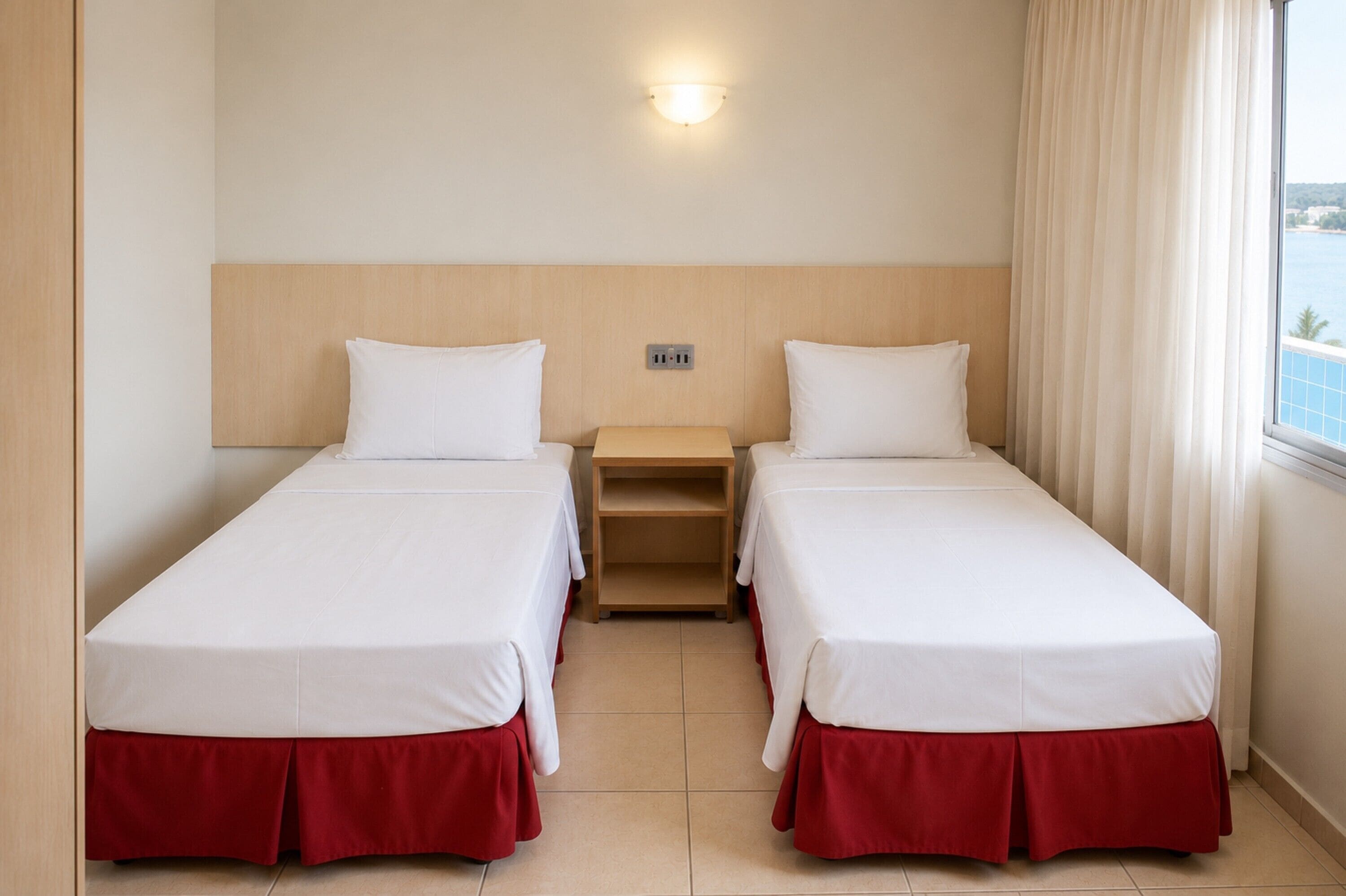 Habitación de hotel con dos camas individuales, una mesita de noche, un enchufe y una ventana con cortinas.