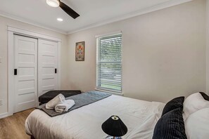 Ein Schlafzimmer mit einem Bett, einem Fenster mit Jalousien, einem Deckenventilator und einer Tür.