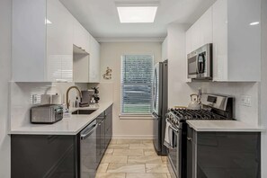 Una cocina moderna con armarios blancos, horno empotrado, estufa, microondas y tostadora.