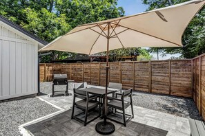 Eine Terrasse mit Tisch, Stühlen, einem Grill und einem großen Sonnenschirm.