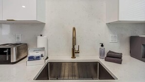 A kitchen with a stainless steel sink, a toaster, a paper towel dispenser, and a bottle of hand soap. - East Austin Home for 4 w/ BBQ Grill, Near DT! (Austin)
