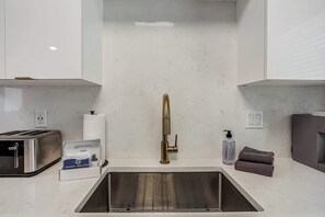 Uma cozinha com uma pia de aço inoxidável, uma torradeira, um dispensador de papel toalha e uma garrafa de sabonete líquido.