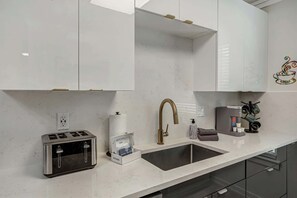 Uma cozinha moderna com torradeira embutida, uma pia de aço inoxidável e uma máquina de café.