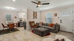A modern living room with a dining area, a gray sofa with orange cushions, a brown leather chair, and a white door with a window. - East Austin Home for 4 w/ BBQ Grill, Near DT! (Austin)