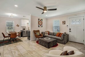 Uma sala de estar moderna com área de jantar, um sofá cinza com almofadas laranja, uma poltrona de couro marrom e uma porta branca com janela.