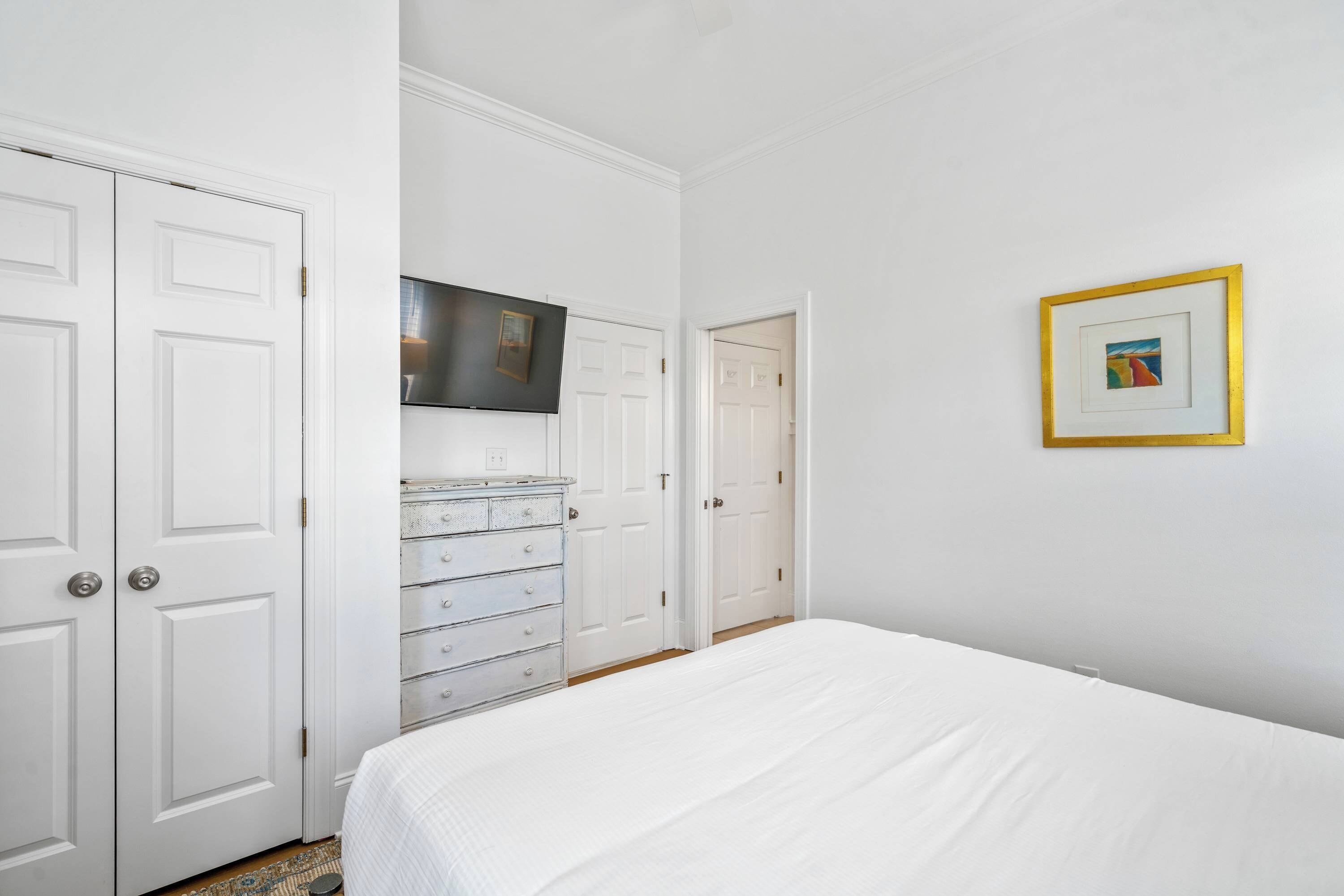 A bedroom with a bed, a dresser, a television, and a framed picture on the wall.