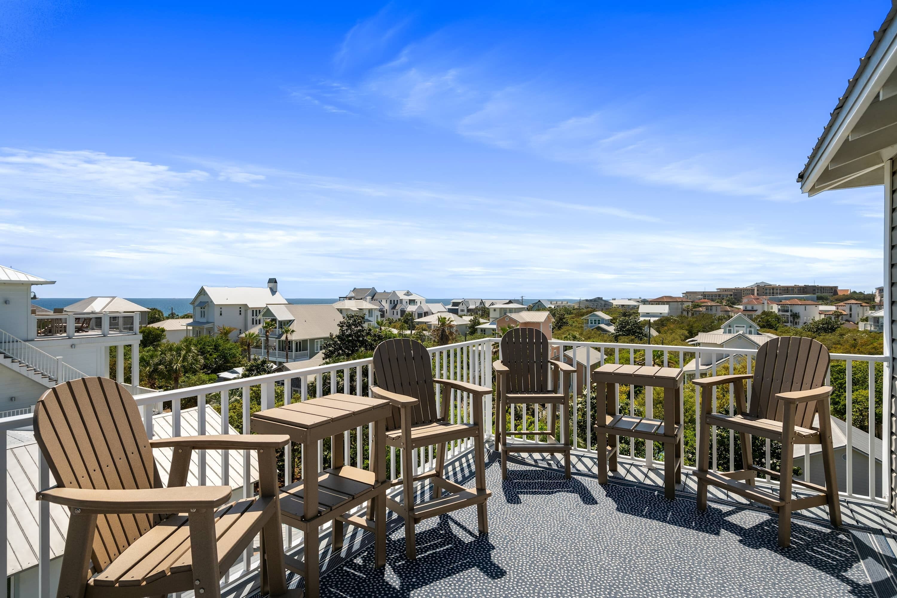 Uma varanda com cadeiras de madeira e piso estampado, com vista para uma área residencial costeira.