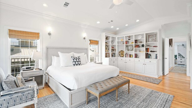 A spacious bedroom with a large bed, a bedside table, a reading chair, a bench, and a built-in wardrobe with shelves. - Blue Mountain View | Private Pool, Rooftop Deck & Bikes (Santa Rosa Beach)