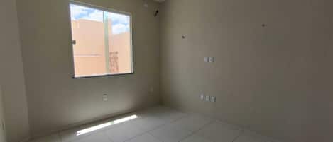 A room with a large window, tiled floor, and light-colored walls.