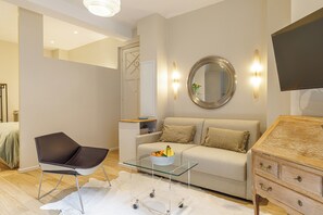 Een moderne woonkamer met een bank, een glazen salontafel, een stoel, een dressoir en een flatscreen televisie aan de muur.