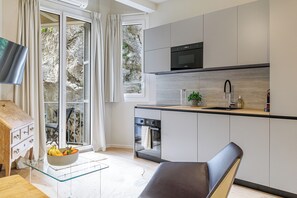 A modern kitchen with a built-in oven, a microwave, and a sink. There is a dining area with a glass table and a chair. - Roch - NEW renovated 1BR w balcony - Castle Hill (Nice)