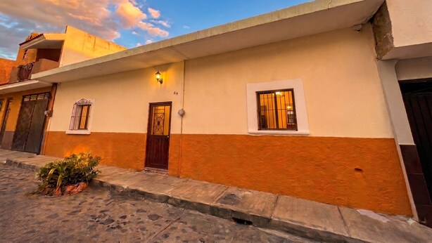 Um edifício com telhado plano, varanda e porta com detalhes decorativos.