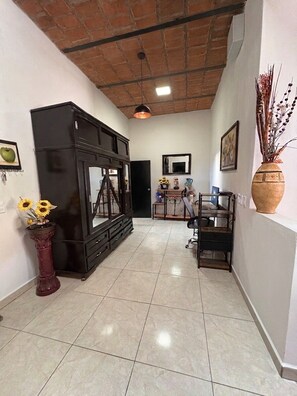 A hallway with a tiled floor, a black cabinet, a desk with a computer, and a vase with sunflowers.