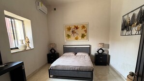 Quarto com cama, ventoinha no teto, janela com vista e obra de arte na parede.