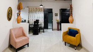 Uma sala de estar ampla com ventilador de teto, dois sofás, uma mesa de jantar e uma cozinha ao fundo.