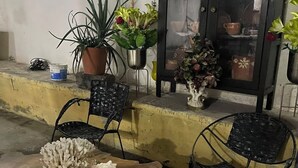 Uma área de pátio com duas cadeiras de metal preto, uma mesa de madeira e um armário com portas de vidro.