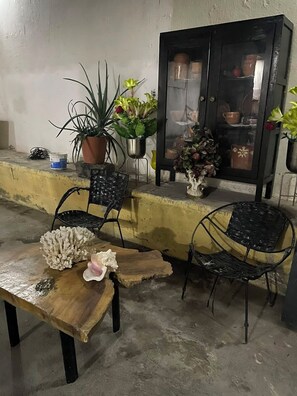 A patio area with two black metal chairs, a wooden table, and a cabinet with glass doors.