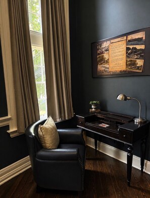A room with a dark blue wall, a desk with a lamp, a leather chair, and a window with curtains.