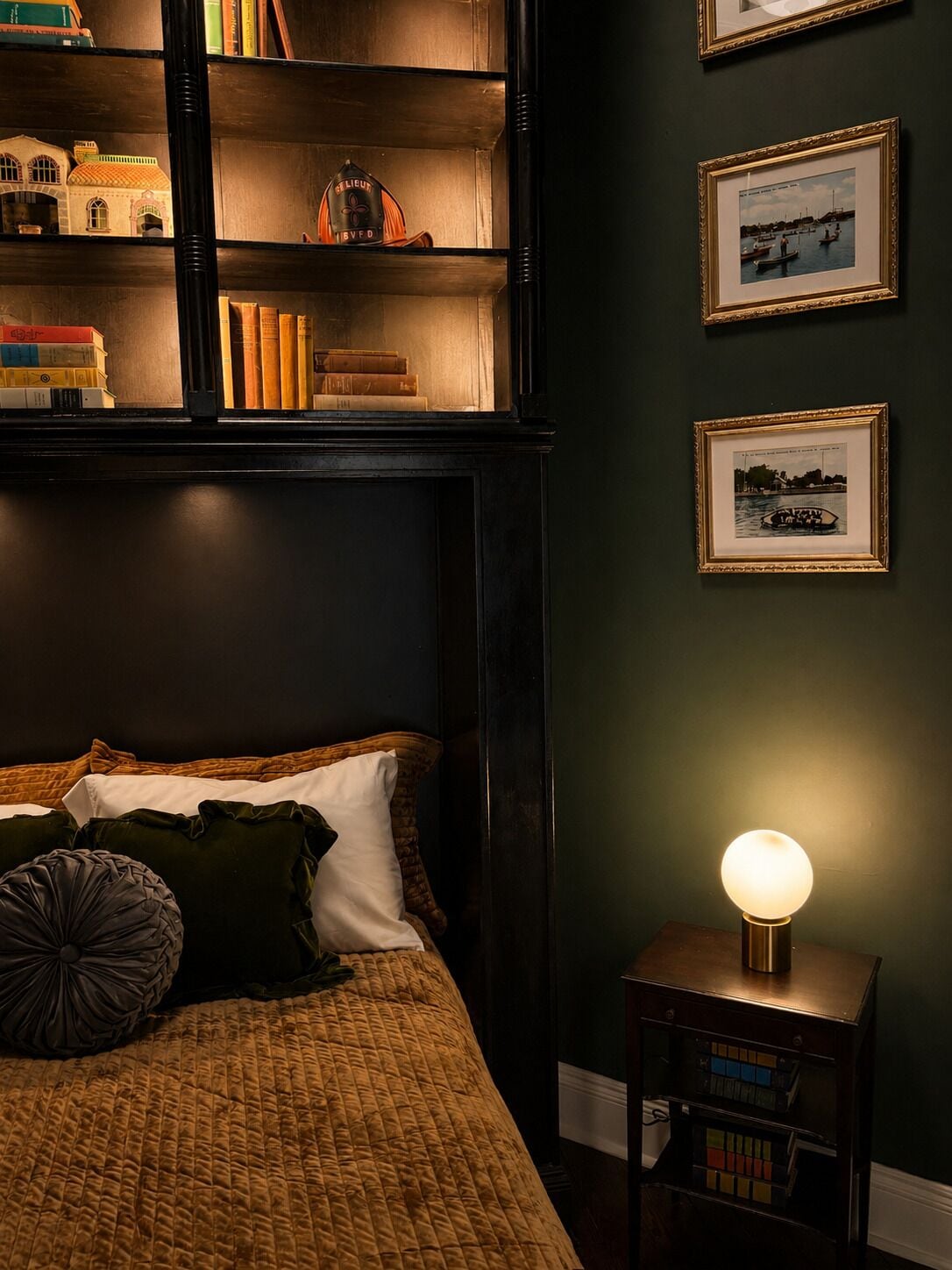 Une chambre à coucher avec un lit, des oreillers, une table de chevet avec une lampe, une bibliothèque et des tableaux encadrés accrochés au mur.