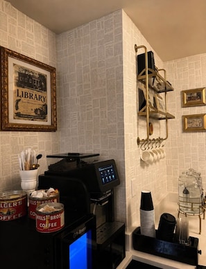 Una estación de café con cafetera, tazas y un bote de café.