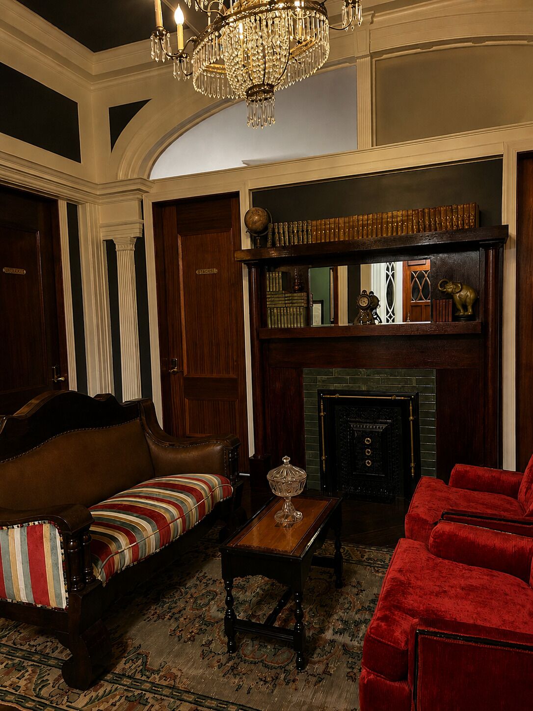 Une pièce au décor traditionnel, avec une cheminée, un canapé rouge, un canapé à rayures, une table basse en bois et un lustre.