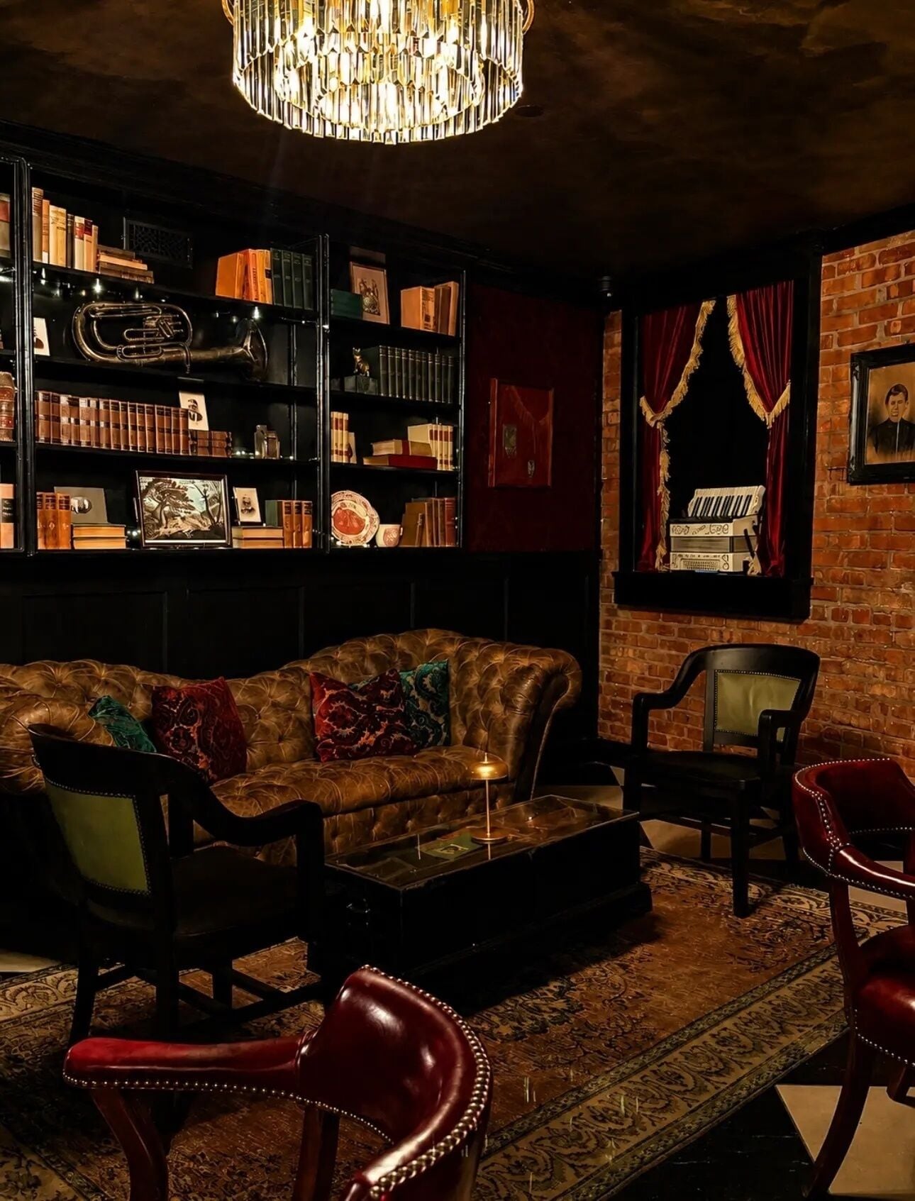 A cozy lounge area with a leather sofa, a bookshelf filled with books and decorative items, a chandelier, and a patterned rug.