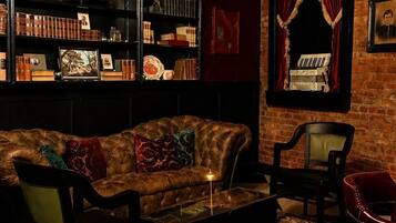 A cozy lounge area with a leather sofa, a bookshelf filled with books and decorative items, a chandelier, and a patterned rug.