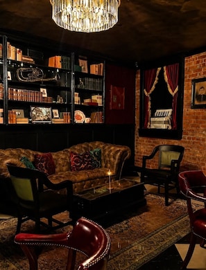 Un rincón tranquilo con un sofá de cuero, una estantería llena de libros y objetos decorativos, una araña y una alfombra estampada.
