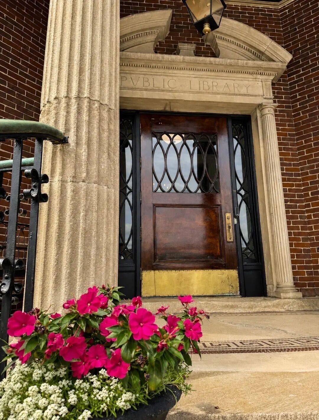 A public library entrance with a dark wooden door, a decorative metal gate, and a column.