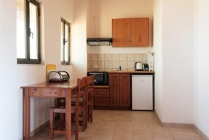 Cocina compacta con armarios de madera, microondas, tostadora y refrigerador pequeño.