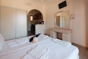 Una habitación de hotel con una cama, un tocador con espejo y una kitchenette al fondo.
